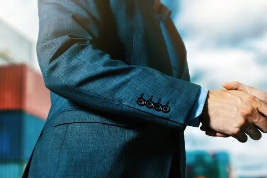 man in suit shaking hands in front of shipping containers