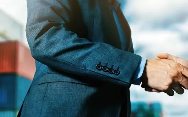 man in suit shaking hands in front of shipping containers